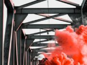 Maloletnik priveden zbog bacanja ručne bombe na lokal u Beogradu Man holding orange smoke bomb on railway bridge, creating a vibrant and dramatic scene.