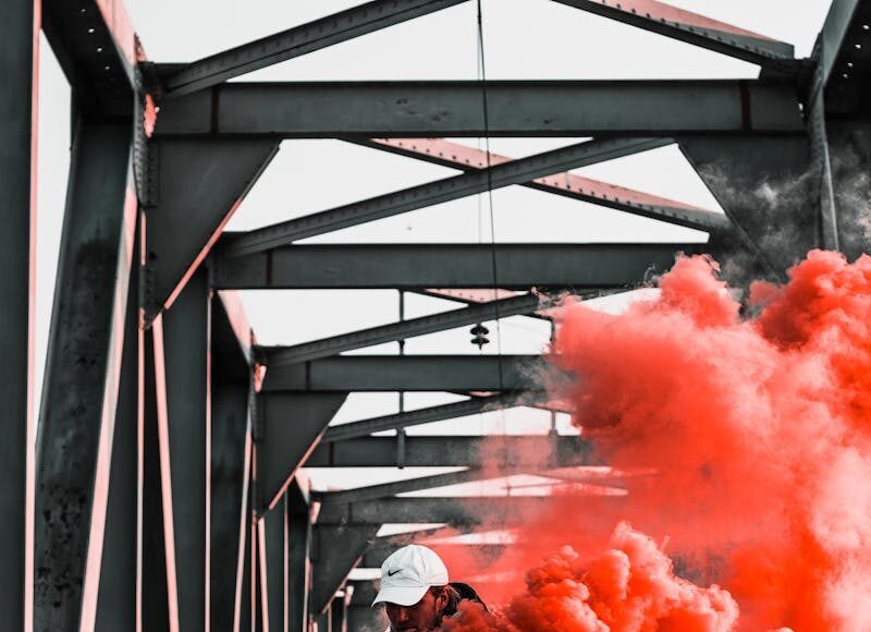 Man holding orange smoke bomb on railway bridge, creating a vibrant and dramatic scene.