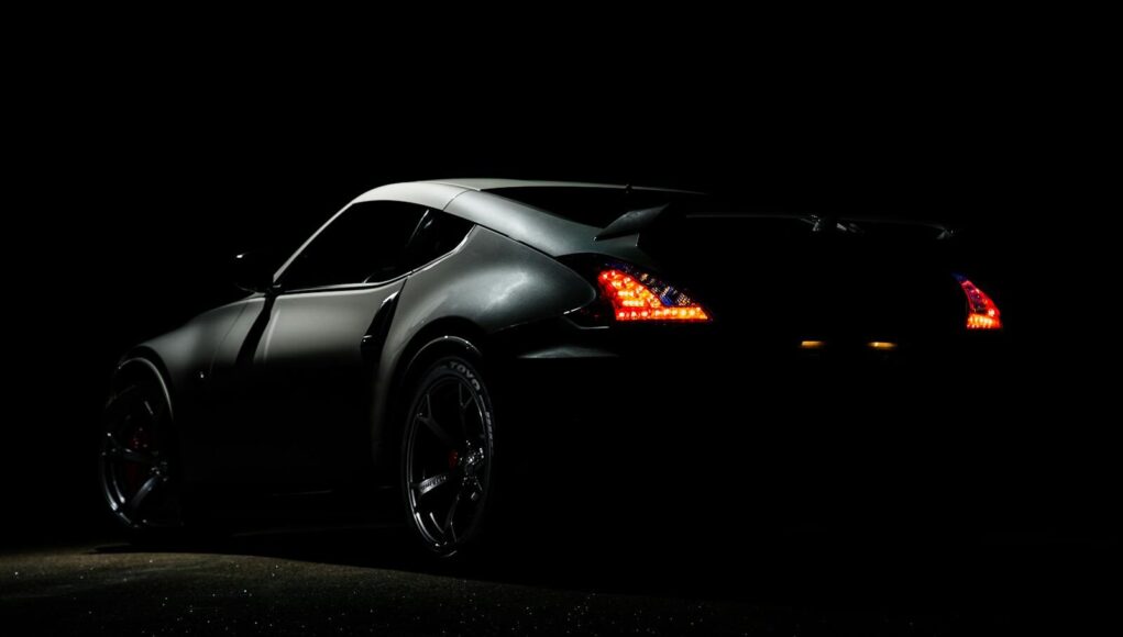 A dramatic shot of a Nissan 370Z sports car illuminated in darkness with vibrant tail lights.
