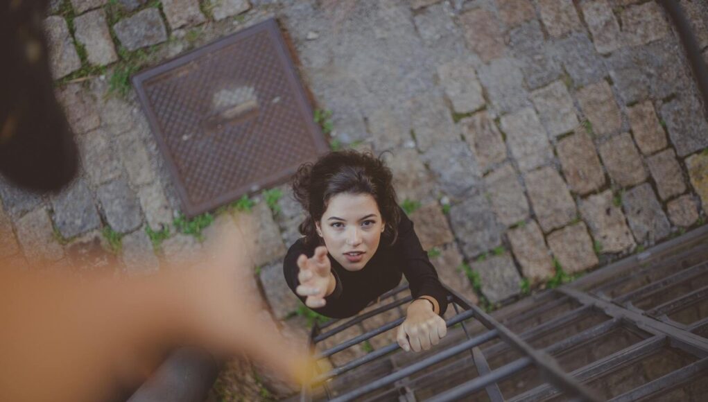 Woman climbs iron ladder outdoors, reaching for help with determination.
