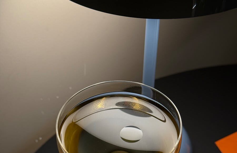 A glass of golden-colored liquid sits elegantly on a black surface, illuminated by soft warm light.