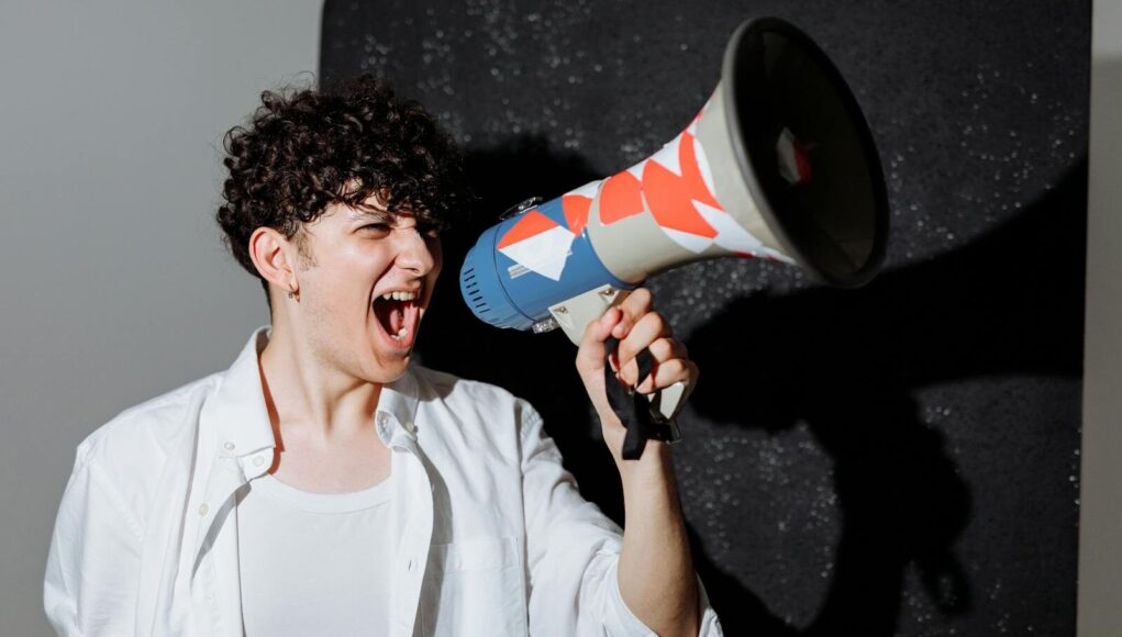 A man passionately shouting through a decorated megaphone, symbolizing activism.