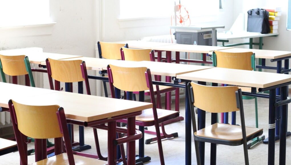 A bright empty classroom with wooden tables and chairs, ready for students.