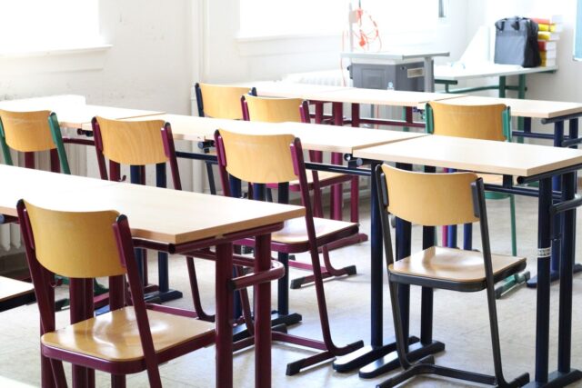 Photo by Ali Ahmad DANESH A bright empty classroom with wooden tables and chairs, ready for students.