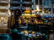 OPREZ, PROMENILI SU TAKTIKU! Nova prevara hara beogradskim kafićima: Pogledajte šta vam spuste na sto pre nego što ostanete bez telefona! A cityscape reflection capturing an urban street scene with a cafe and modern architecture.