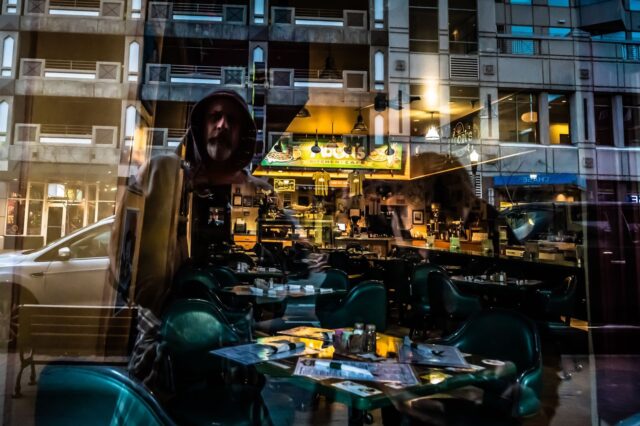Photo by Brett Sayles A cityscape reflection capturing an urban street scene with a cafe and modern architecture.