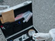 Kako funkcioniše forenzika? Tragovi koji otkrivaju počinioca A forensic investigator handles a test tube at a crime scene with an open evidence collection suitcase on the ground.
