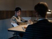 Prevare koje su nasmejale internet: Od „nigerijskog princa“ do lažnih milionera – evo kako da ih prepoznate Tattooed man in white tank top and cap during intense police interrogation in dimly lit room.