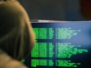 Epidemija digitalnih prevara: Kako prevaranti kradu novac u nekoliko klikova i zašto ih je teško pronaći Person wearing a hoodie typing code on a computer screen with green text, depicting hacking scene.