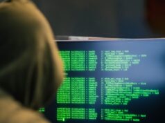 Epidemija digitalnih prevara: Kako prevaranti kradu novac u nekoliko klikova i zašto ih je teško pronaći Person wearing a hoodie typing code on a computer screen with green text, depicting hacking scene.