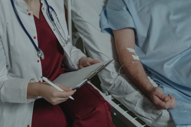 Photo by Tima Miroshnichenko Doctor reviewing medical chart while assisting a patient in a hospital bed.