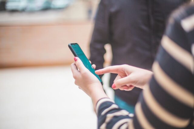 Close-up of a person's hand using a smartphone outdoors on a bright day.