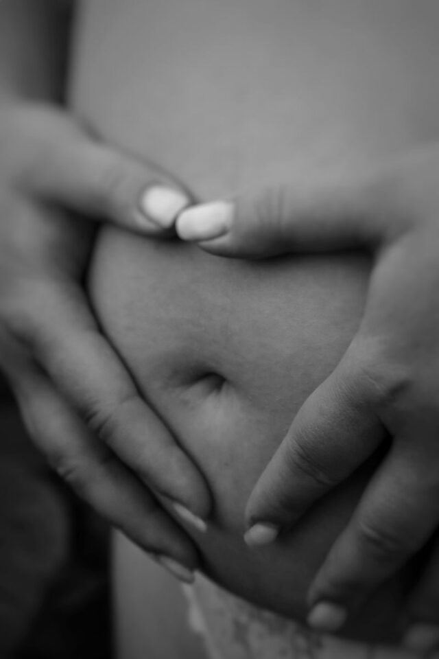 Photo by Katya Puzanova Monochrome close-up of hands gently embracing a pregnant belly.