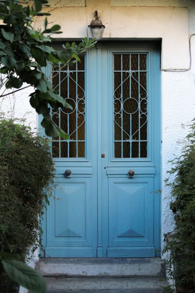 Photo by Lucas Negredo Sagarzazu Charming blue doors with decorative ironwork in Hendaye, France, surrounded by greenery.