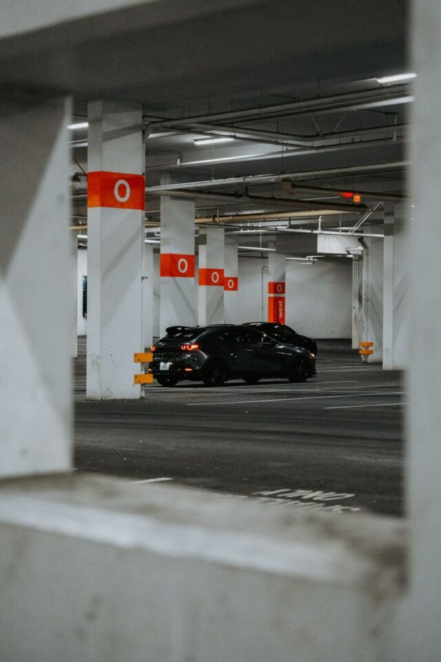 Photo by Luke Miller A stylish black sports car parked in a modern, empty urban parking garage.