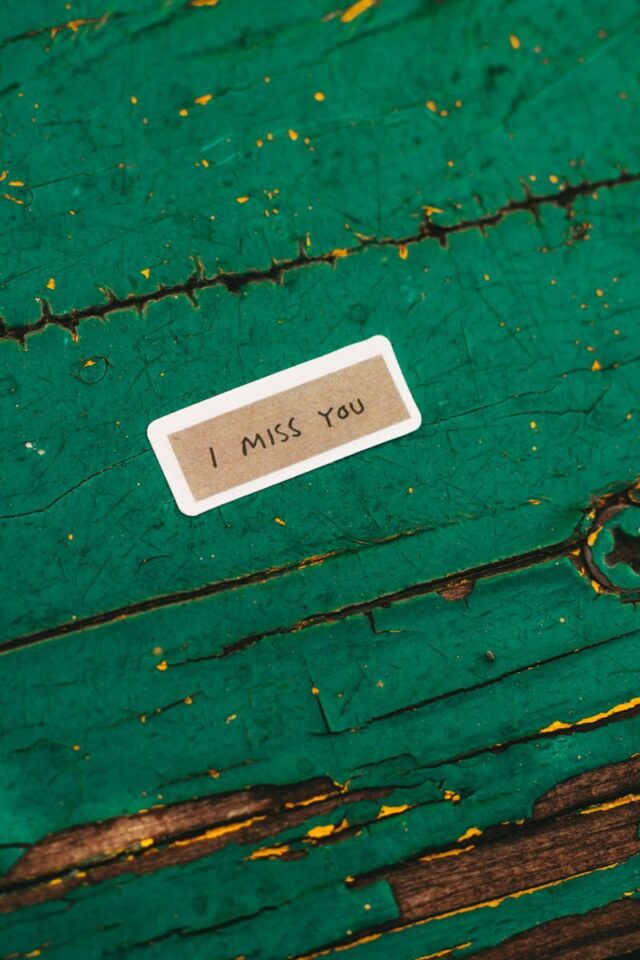Photo by Зоряна Русин Small I miss you note on aged green wooden surface, evoking nostalgia.